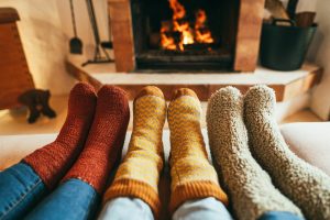 A view of a family’s socked feet as they sit close together in front of a fire, comfortable in their knowledge of how to prevent winter fire hazards.