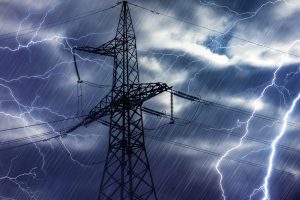 A voltage tower and powerlines are backlit by lightning, emphasizing the importance of storm prep and generator installation.