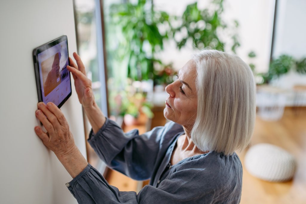 Image of an older woman interacting with a home automation device on the wall.