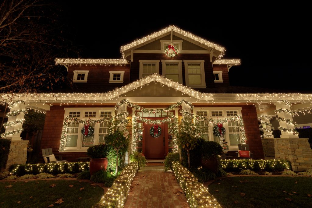 The front of a home, with the railings, bushes, and trees modestly lit for the winter holidays.
