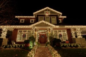 The front of a home, with the railings, bushes, and trees modestly lit for the winter holidays.