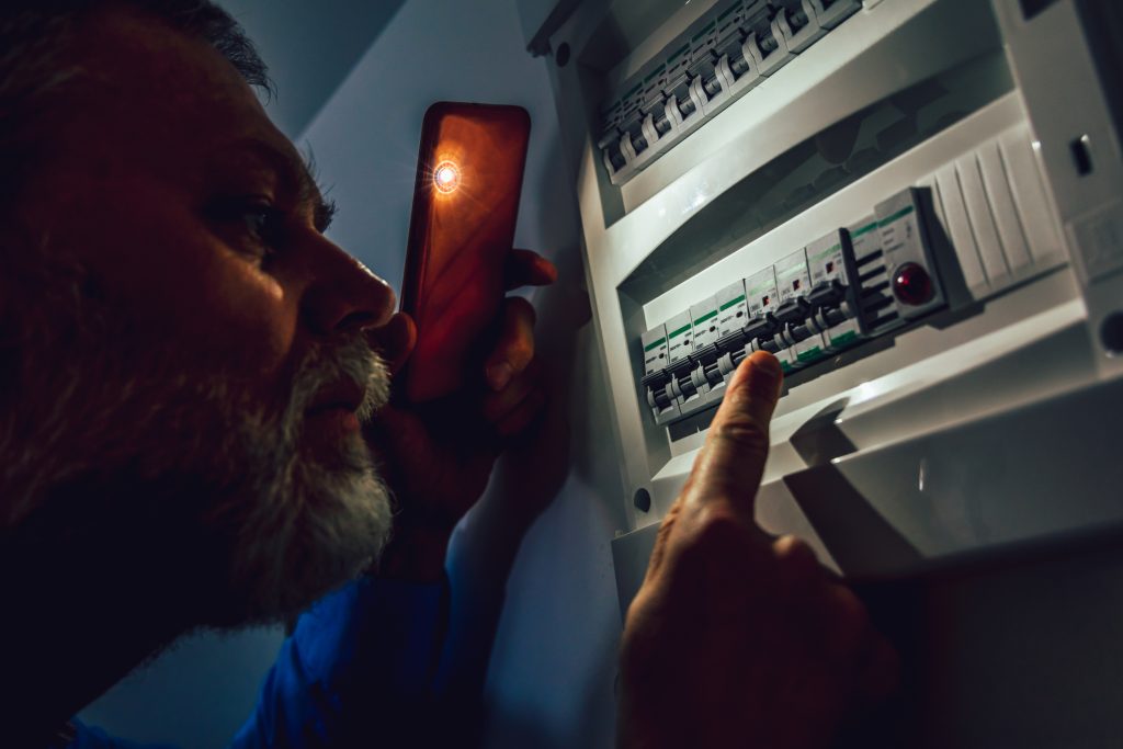 A homeowner inspects his circuit breaker after a power outage due to a tripped breaker.
